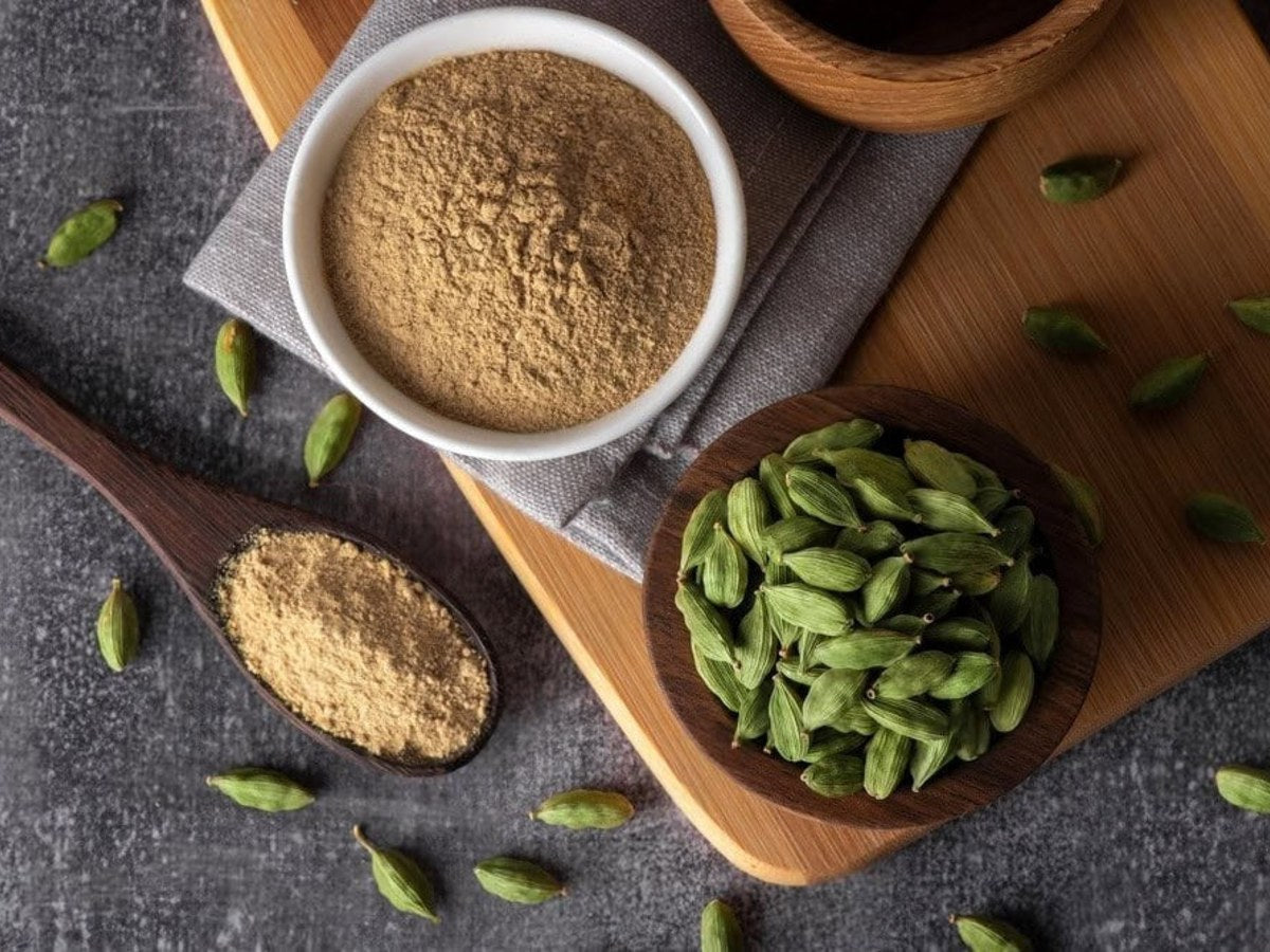 Ground Arabic coffee with green cardamom pods in bowls on a wooden board
