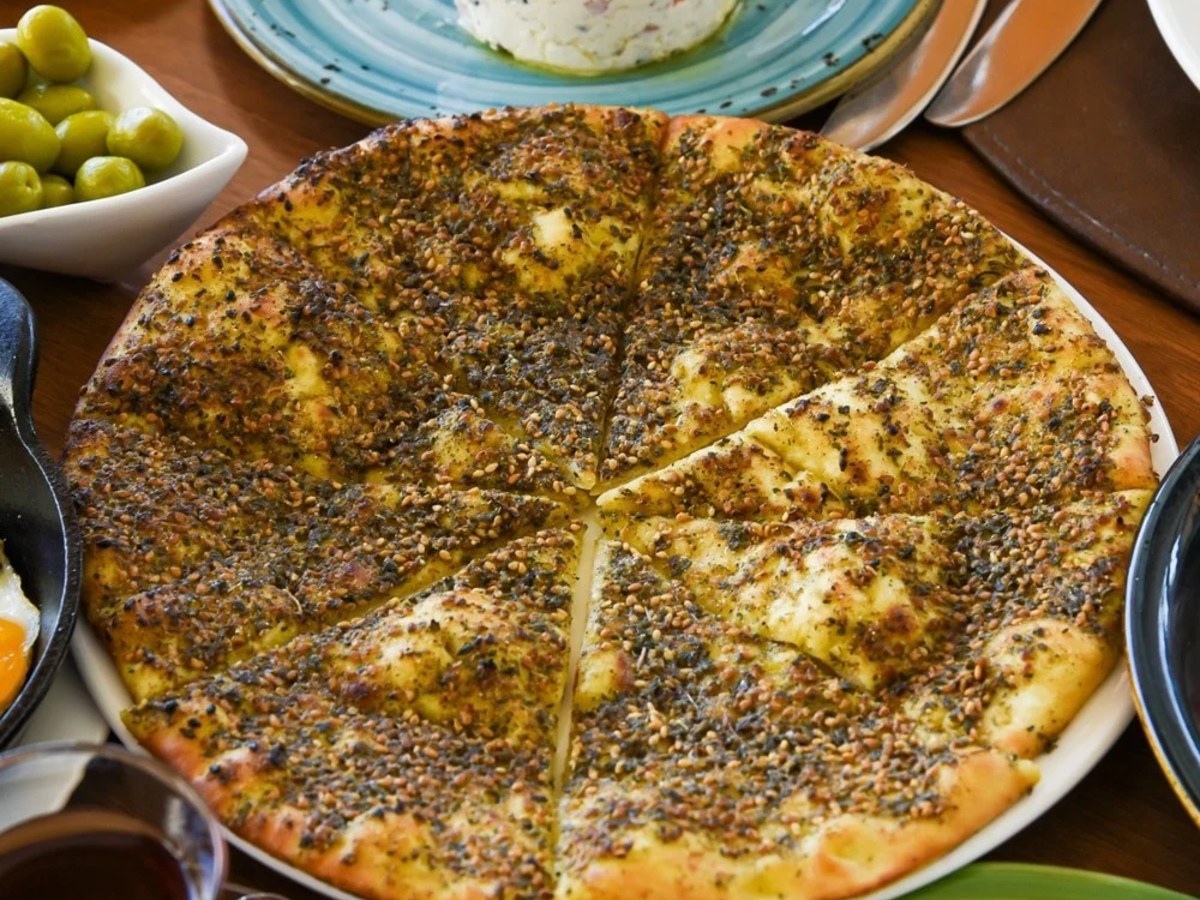 Za’atar manakish flatbread cut into slices, with a bowl of green olives