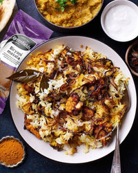 Plate of chicken biryani with fried onions beside a Greenfields biryani masala pack