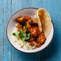 Bowl of tikka masala with rice and naan on a blue table