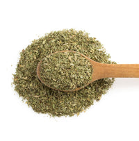 Dried basil in a wooden spoon on a pile of dried basil