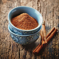 Blue bowl of ground cinnamon with cinnamon sticks