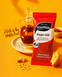 Greenfields Aleppo chilli pack beside a jug of oil on a yellow background