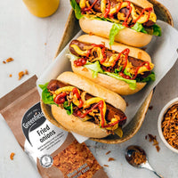Hot dogs topped with crispy fried onions beside a Greenfields pack