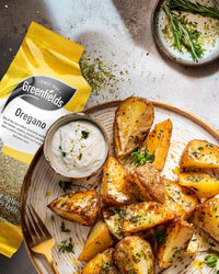Roast potatoes sprinkled with oregano beside a Greenfields oregano pack