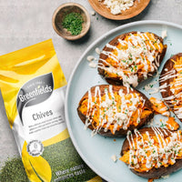 Baked potatoes with soured cream and chives beside a Greenfields chives pack