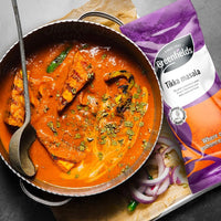 Pan of tikka masala curry beside a Greenfields tikka masala pack