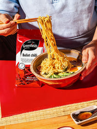 Noodles lifted from a bowl beside a Greenfields bullet chilli pack